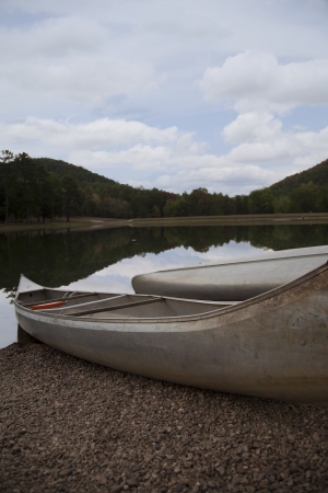 Two silver canoes sit in the gravel bed by a lake with the reflection of a blue sky の写真素材