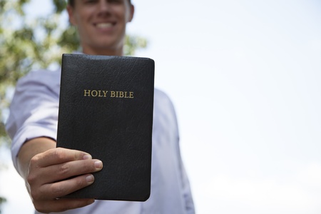 A young man stands outside while holding out a bible in front of him.の写真素材