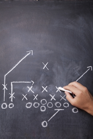 A hand draws a football play on a chalkboard with chalk leaving room for copy の写真素材