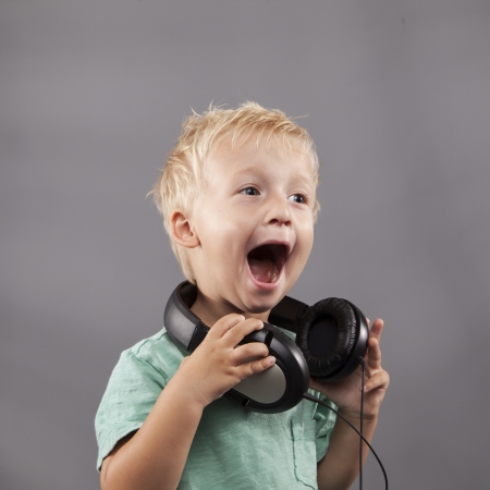 A happy young boy with headphones around his neck sings loudly.の写真素材