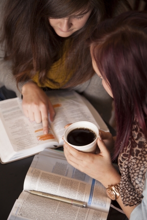 Two young women study the bible together while drinking coffee.の写真素材