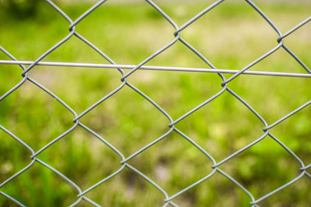 Wire fence out of metal enclosure fence around grass field with green background and bushes and grass with woven fence.の写真素材