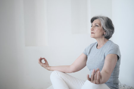 An elderly senior woman sitting in lotus pose in her home zen stone gardenの写真素材