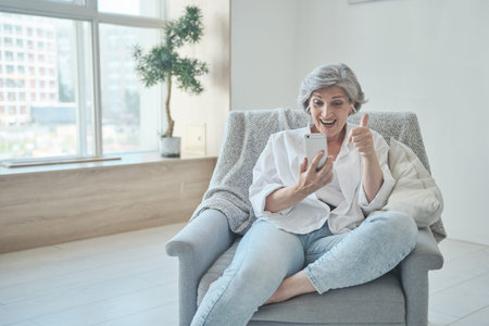 Happy senior old woman in headphones looking mobile screen, enjoying video meeting