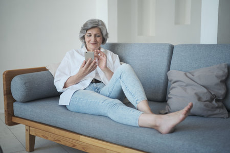 Relaxed smiling mature senior lady in her 60s using smartphone,の写真素材