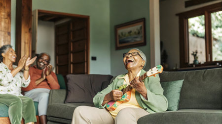 Happy senior woman playing ukulele and singing for friends at homeの素材