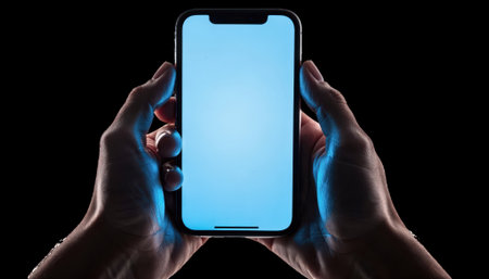 Closeup of hands holding a glowing smartphone with blue light reflecting on skin isolated on white symbolizing device use before sleep.の素材