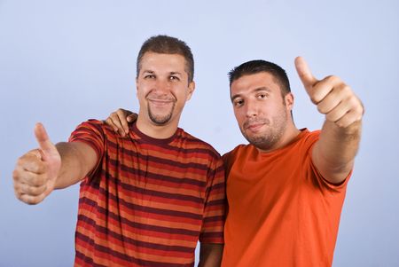 Successful friends giving thumbs up and wearing orange blank t-shirt on blue backgroundの写真素材