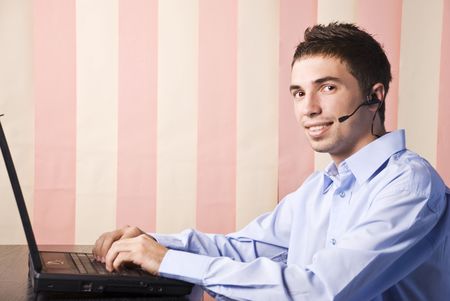 Young man customer service sitting at desktop with laptop and headphones ready to hel you,vertical blinds backgroundの写真素材