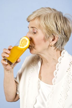 Healthy senior woman standing in profile and drinking a glass with fresh orange juice on blue backgroundの写真素材