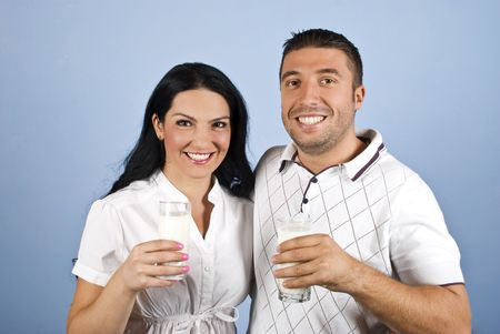 Happy couple healthy holding glasses with milk and standing together in a hug showing smiles for you on blue backgroundの写真素材