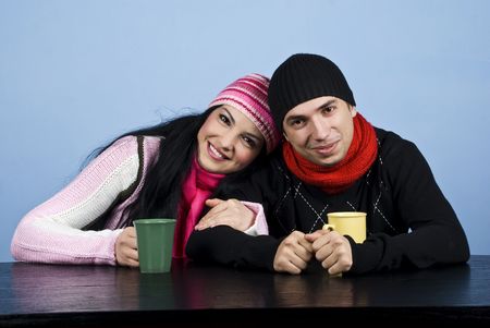 Affectionate couple  dressed in warm clothes sitting at table and enjoying together a hot drink over blue backgroundの写真素材