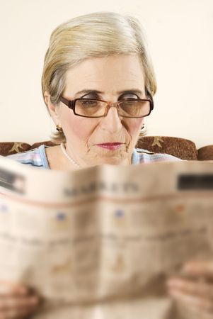 Senior woman with eyeglasses reading the news in her homeの写真素材