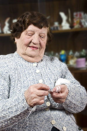 Elderly woman 80s knitting and  sitting on chair in her house