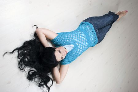 Top view of beautiful brunette with long hair lying down with hands under her head and relaxing on white wooden floor in new houseの写真素材