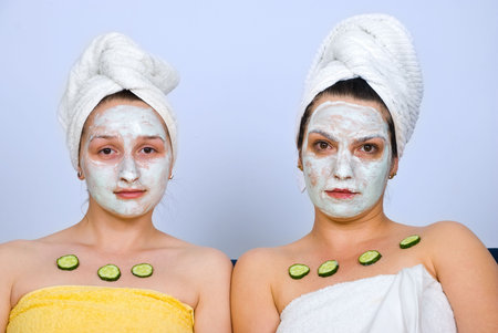 Close up of two women with facial mask and slices cucumber on chest at spa resort