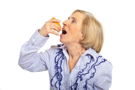 Senior woman squeeze half of orange in her open mouth  isolated on white backgroundの写真素材