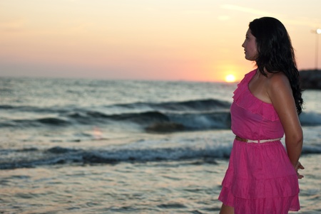 Beautiful tan woman on beach at sunset looking awayの写真素材