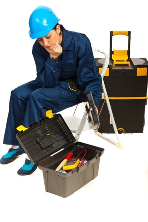 Thinking worker woman looking in a tools box  and sitting on step ladder isolated on white backgroundの写真素材