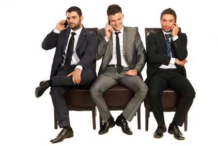 Three business men sitting on chairs in a line and speaking by phones mobile isolated on white backgroundの写真素材