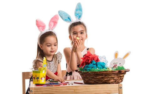 Two little girls in kindergarten sitting at table and painting and decorating Easter eggs