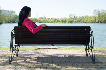 Sad woman sitting on bench in park looking to the waterの写真素材