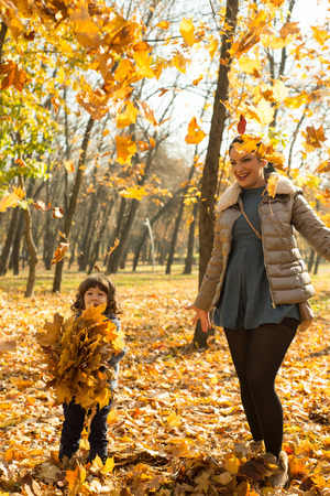 Cheerful mother and son tossing autumn leaves in park and having fun togetherの写真素材