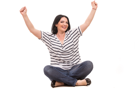 Successful casual woman sitting with legs crossed and raising her fists isolated on white backgroundの写真素材