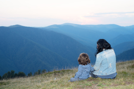 Back of mother and son sitting on grass in the mountains and having conversationの写真素材