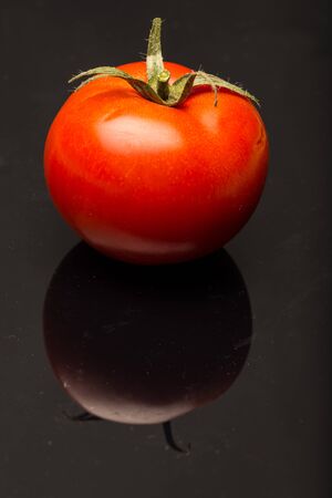 Single whole tomato against black background with reflectionの写真素材