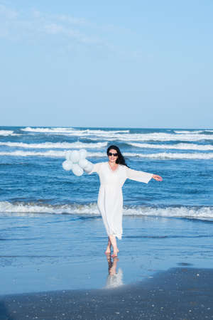 Beauty woman at sea with white balloons make spinsの写真素材