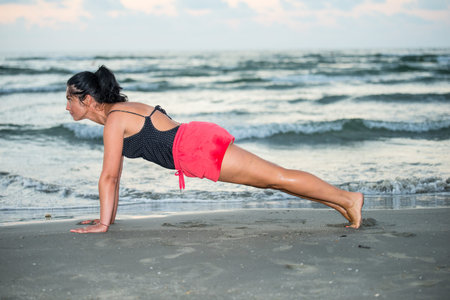 Beauty brunette woman making some fitness exercises on the beach at sea