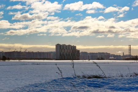 Winter morning landscape with a field covered with snow and city houses in the distance opposite the bright blue skyの写真素材