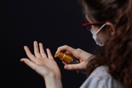 hand hygiene for viral infections, young girl in an antiviral medical respiratory mask puts on her hands an antiviral, antiseptic hand spray on a dark gray background.の写真素材