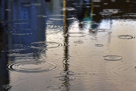 Drops of rain bubbling in a puddle with the reflection of light.の写真素材