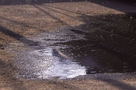 Drops of rain bubbling in a puddle with the reflection of light.の写真素材