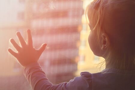 Child at the window counts down the days of quarantine against the background of the cityの写真素材