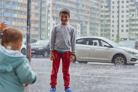 a child in the rain rejoices in a sudden heavy rain, city children.の写真素材