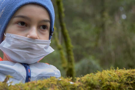 boy in protective sterile medical mask on his face looking at camera outdoors.の写真素材