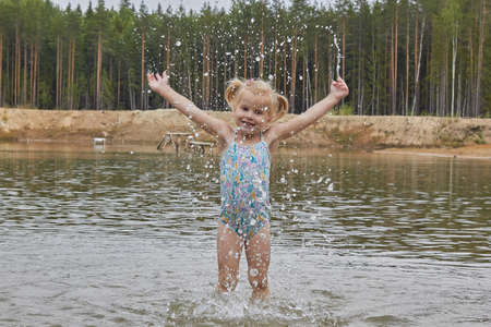 little girl in the water on the lake in the forest spray drops in nature.の写真素材