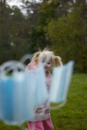 A little blonde girl on the street in the park in the fall, throws throws medical masks.の写真素材