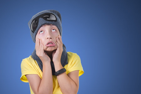 The child is tired and bored in a hat and scarf on a light blue background.
