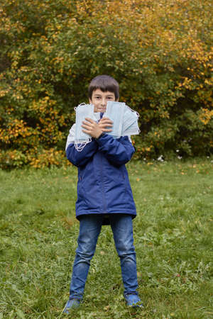 Young boy in park in autumn amid yellow leaf tossing medical disposable masksの写真素材