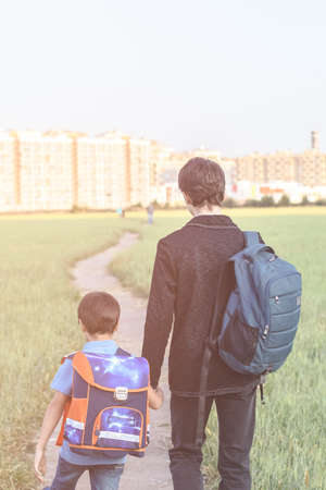 Brothers go to school. The teenager and his younger brother with backpacks hold hands, brothers smile happy faces of children. back to schoolの写真素材
