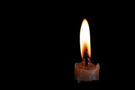 On a black background, the bright light of the candle burns down brightlyの写真素材