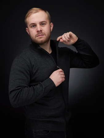 vertical portrait of a waist length blond man on a dark background, in a jacket