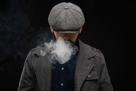 a bearded stylish man smoking a pipe man smokes a pipe on a dark backgroundの写真素材