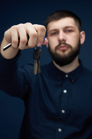 a man with a beard in his hand car keys on a dark background