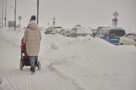A lady with a stroller walks through the snow-covered streets in winter, its cold and freezing.の写真素材