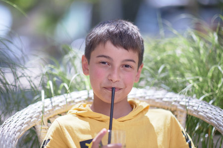 portrait of a child, burnt skin in the sun, a 10-year-old brunette boy in a summer cafe. Drinks a...